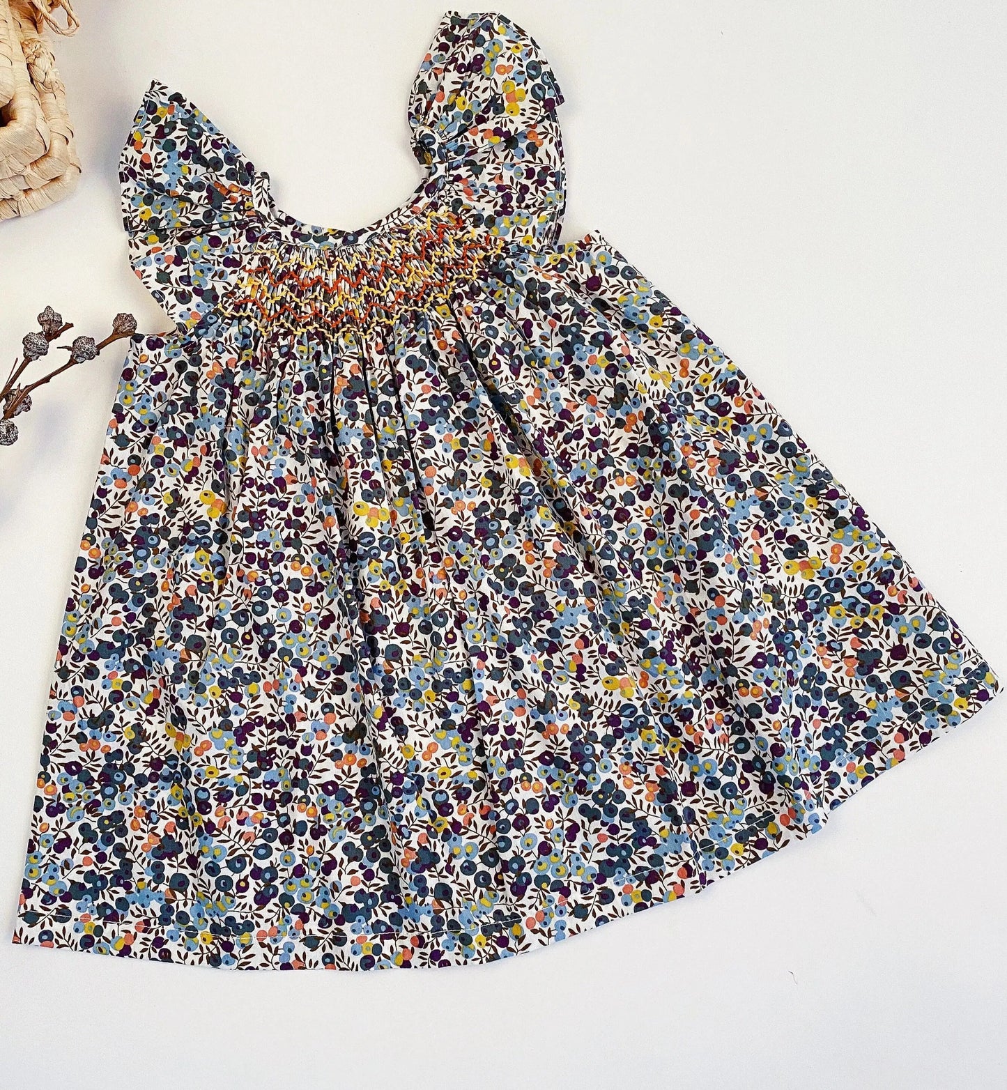 Colorful small Print, Cream background with Navy, Yellow, Light blue and peachy color. Smocking is delicately done in Yellow, Red and white. Flyaway sleeves lend a fun, summery feel.
